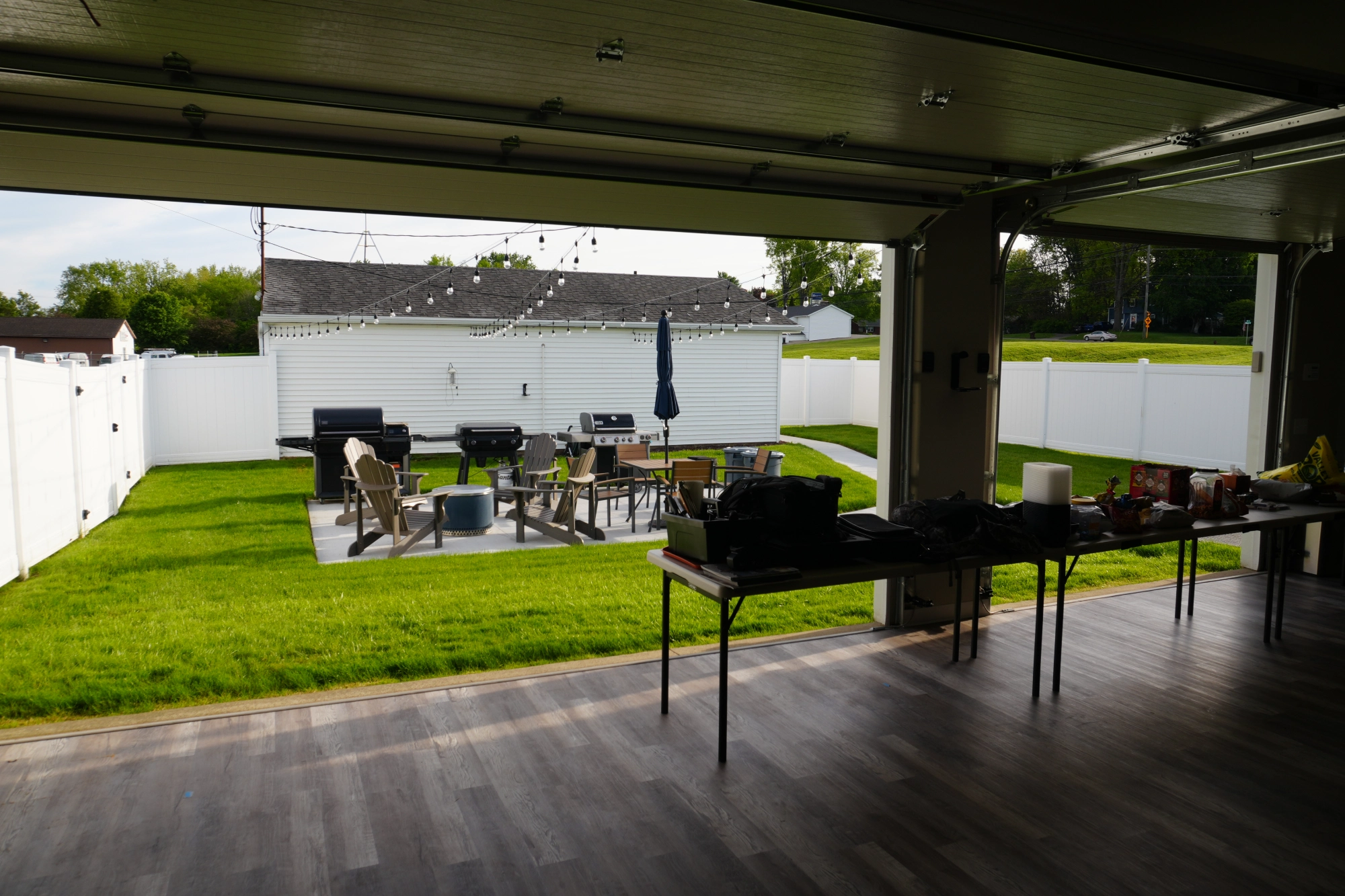 Open garage overlooking fenced backyard patio with grill